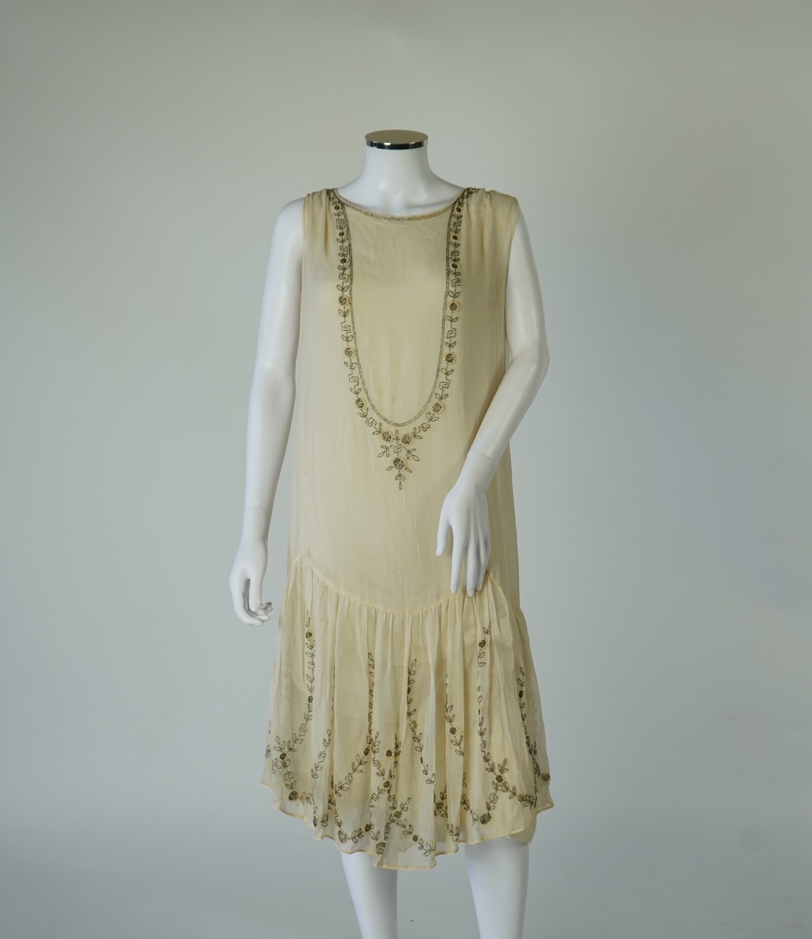 A 1920's cream silk georgette three quarter length, silk lined ‘flapper dress’. Designed with beaded and pearl floral embroidery, a stylish long beaded keyhole slit at the back, a beaded front bodice and flying beaded pa